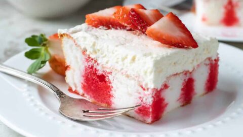 A slice of strawberry jello poke cake on a white plate.
