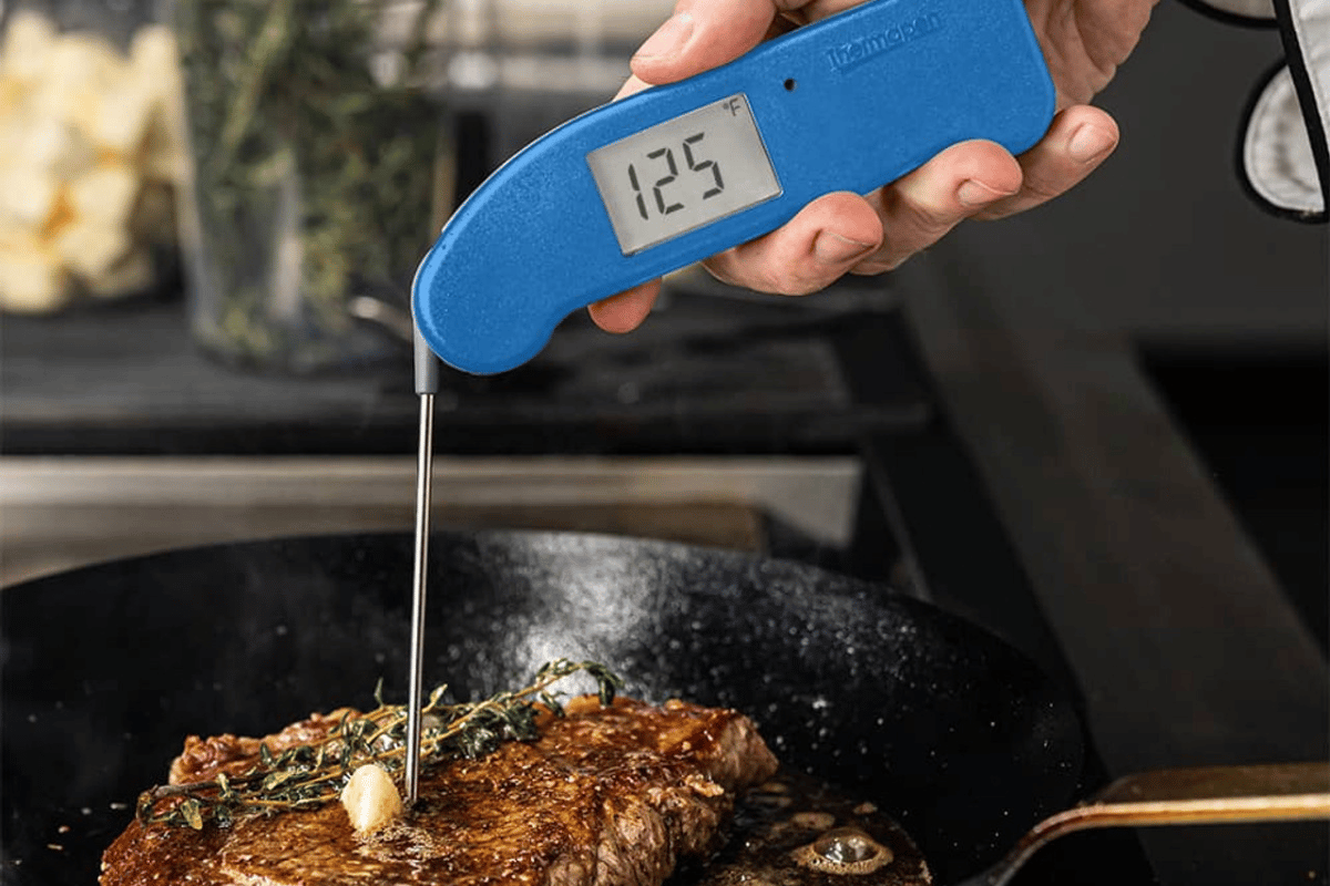 A thermapen temping a steak in a cast iron skillet.