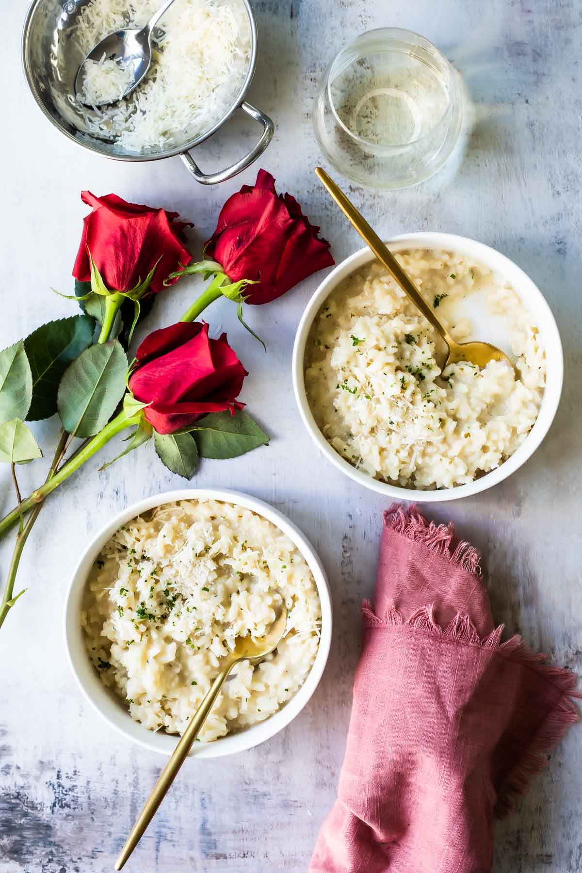 2 bowls full of Risotto with red roses and white wine next to them.