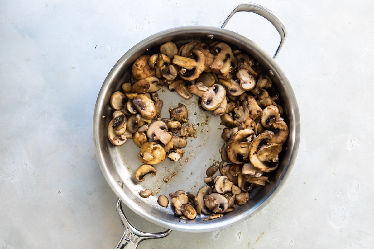 Mushrooms and garlic being cooked in a silver skillet.
