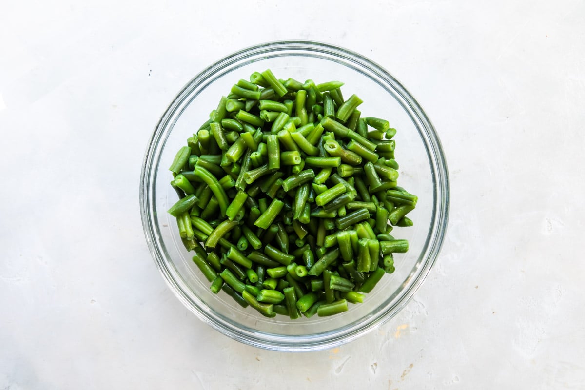 A clear glass bowl with cut green beans in it.