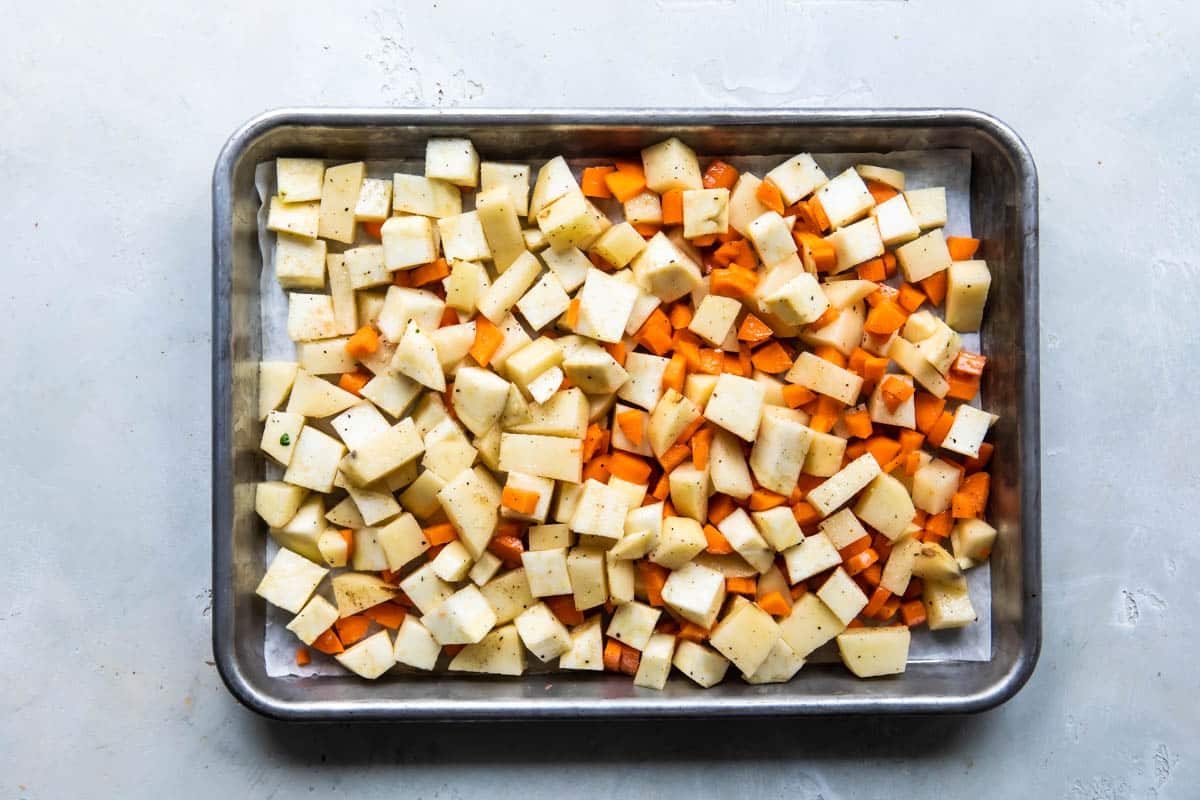 Carrots and potatoes on a baking sheet before being roasted.