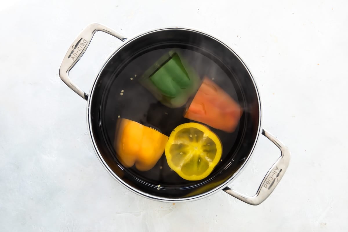 Four bell peppers being boiled in a stock pot.