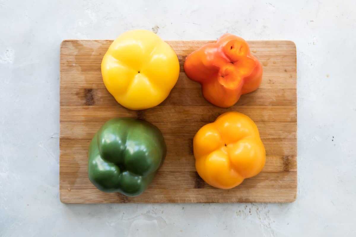Four colored bell peppers on a wooden cutting board.