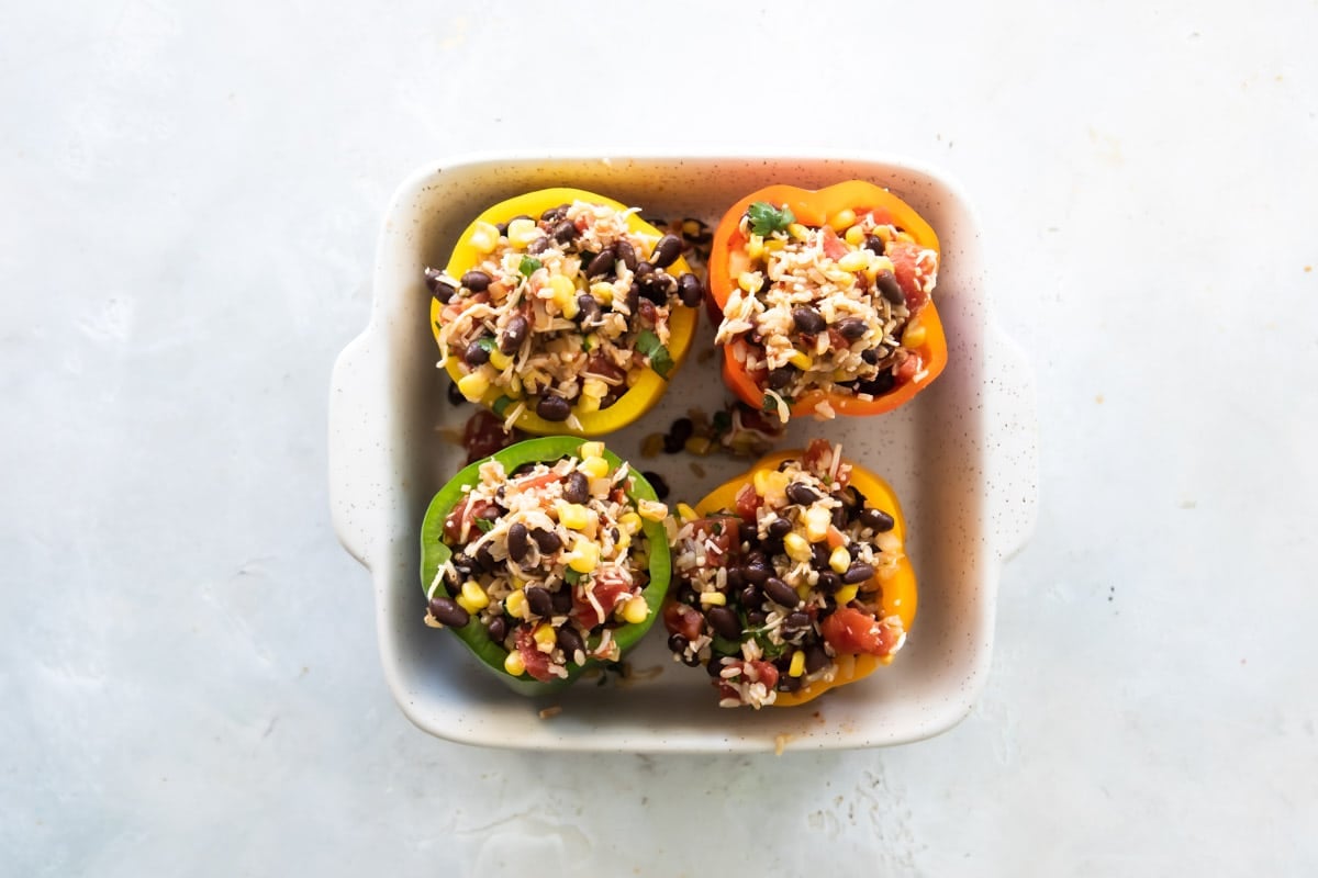 Vegetarian stuffed peppers in a white baking dish before being topped with cheese.