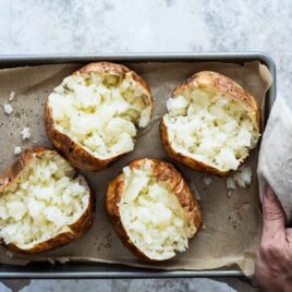 Someone holding a pan with four air fryer baked potatoes.