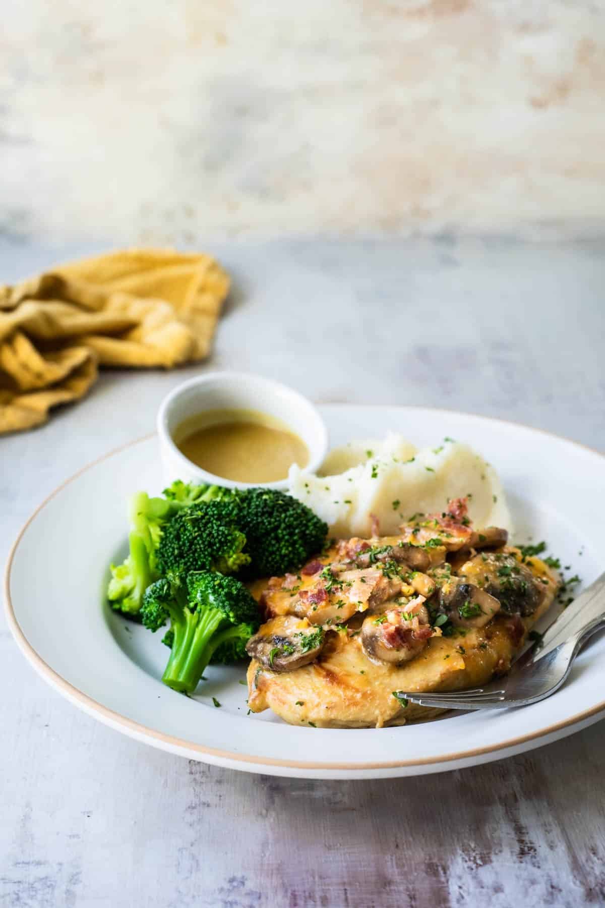 Alice Springs chicken on a white plate with sides of broccoli and mashed potatoes.