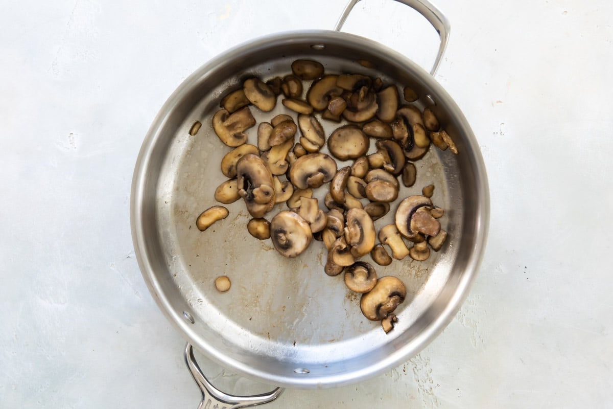 Mushrooms cooking in a metal skillet.