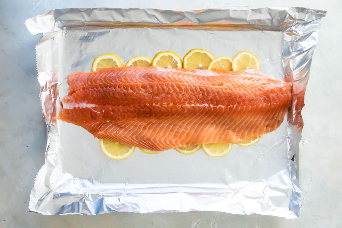 A large side of raw salmon sitting on a layer of lemon slices on top of foil on a baking sheet.