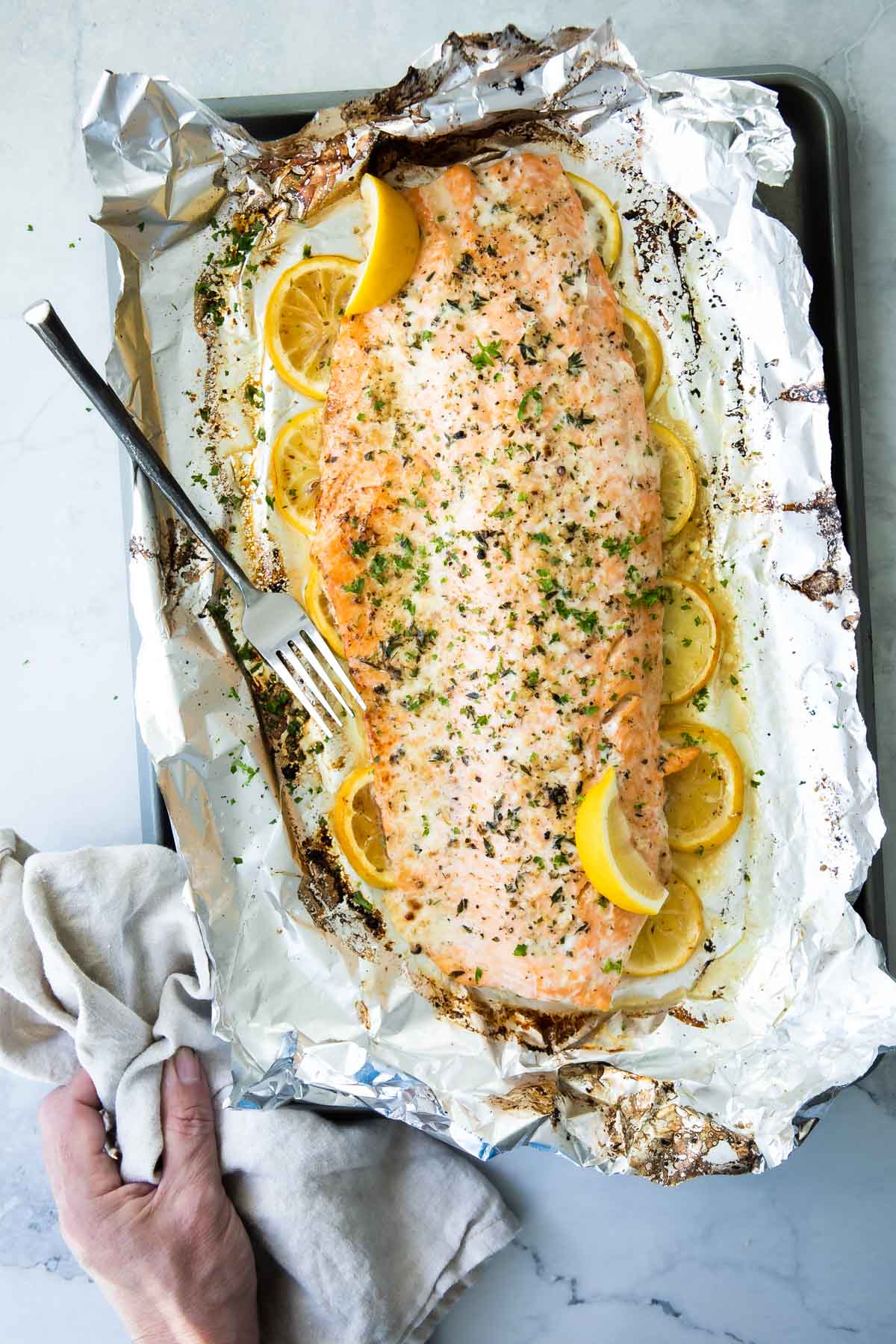 A large side of cooked salmon with spices on top sitting on a layer of lemon slices on top of foil on a baking sheet.