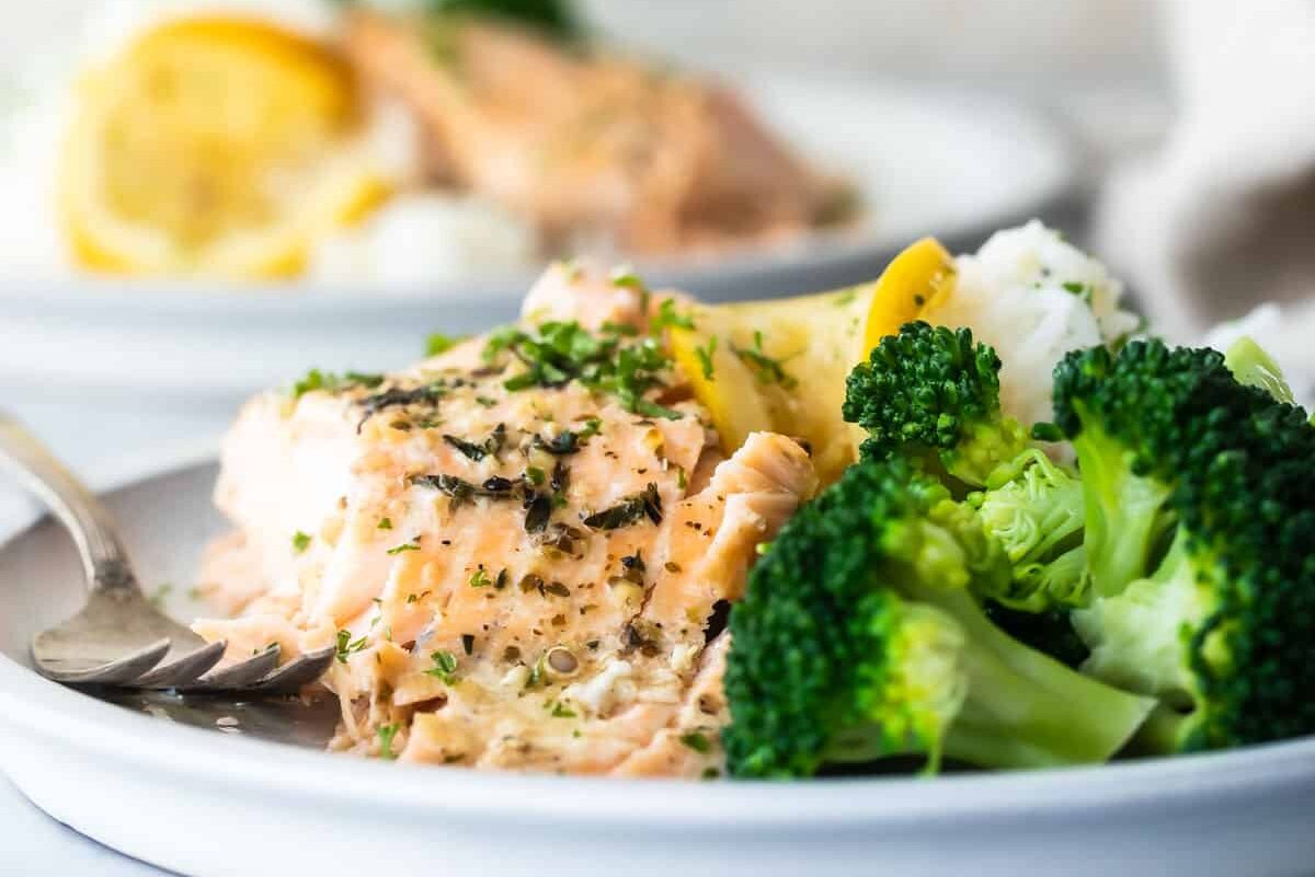 A piece of baked salmon on a plate with white rice and roasted broccoli.