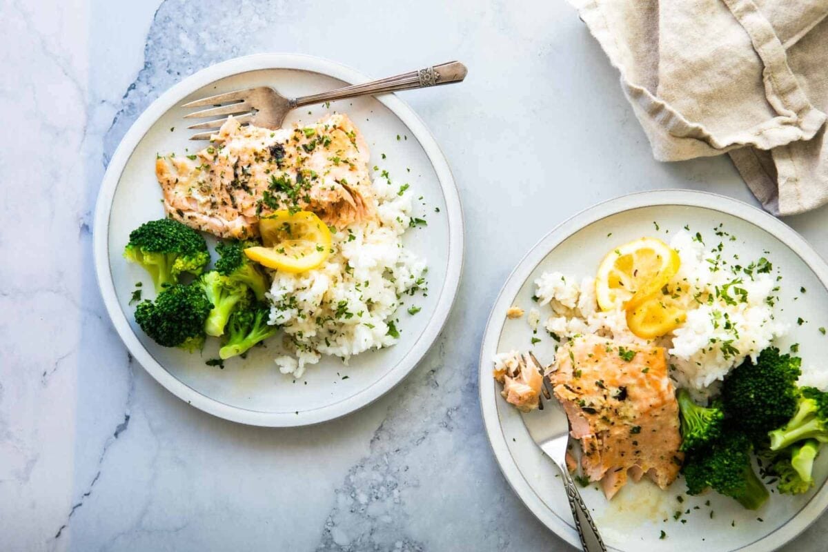 A piece of baked salmon on a plate with white rice and roasted broccoli.
