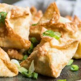 Crab rangoons on a brown platter topped with green onions.