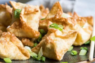 Crab rangoons on a brown platter topped with green onions.