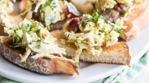 A white plate on top of a green napkin with toasts that have curried chicken salad on top of them.