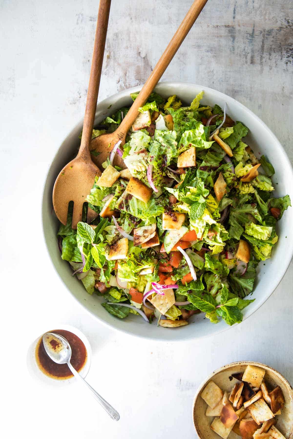 A serving bowl of fattoush salad with wooden serving utensils.