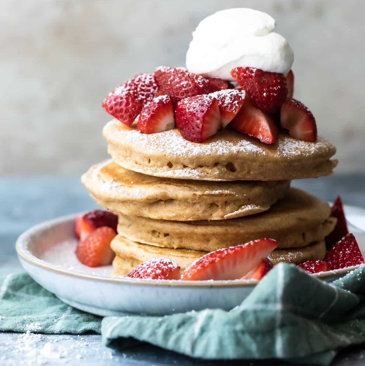 A stack of healthy pancakes with strawberries, whipped cream and powdered sugar.