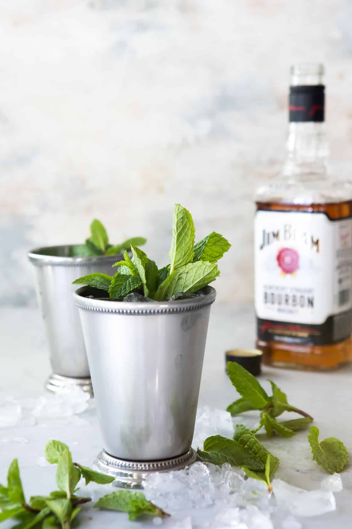 Two mint juleps in silver cups and a bottle of Jim Beam.