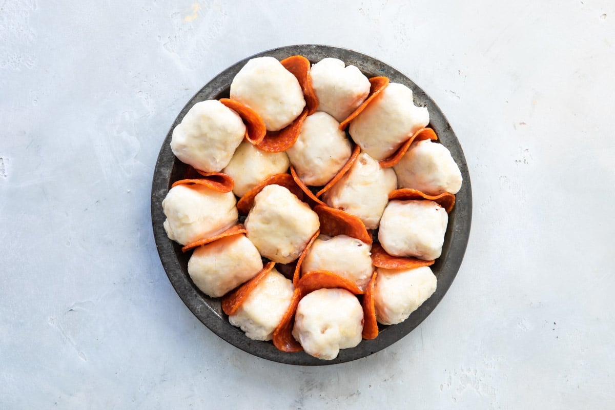 Pepperoni pizza bites in a dark gray pan before being baked.
