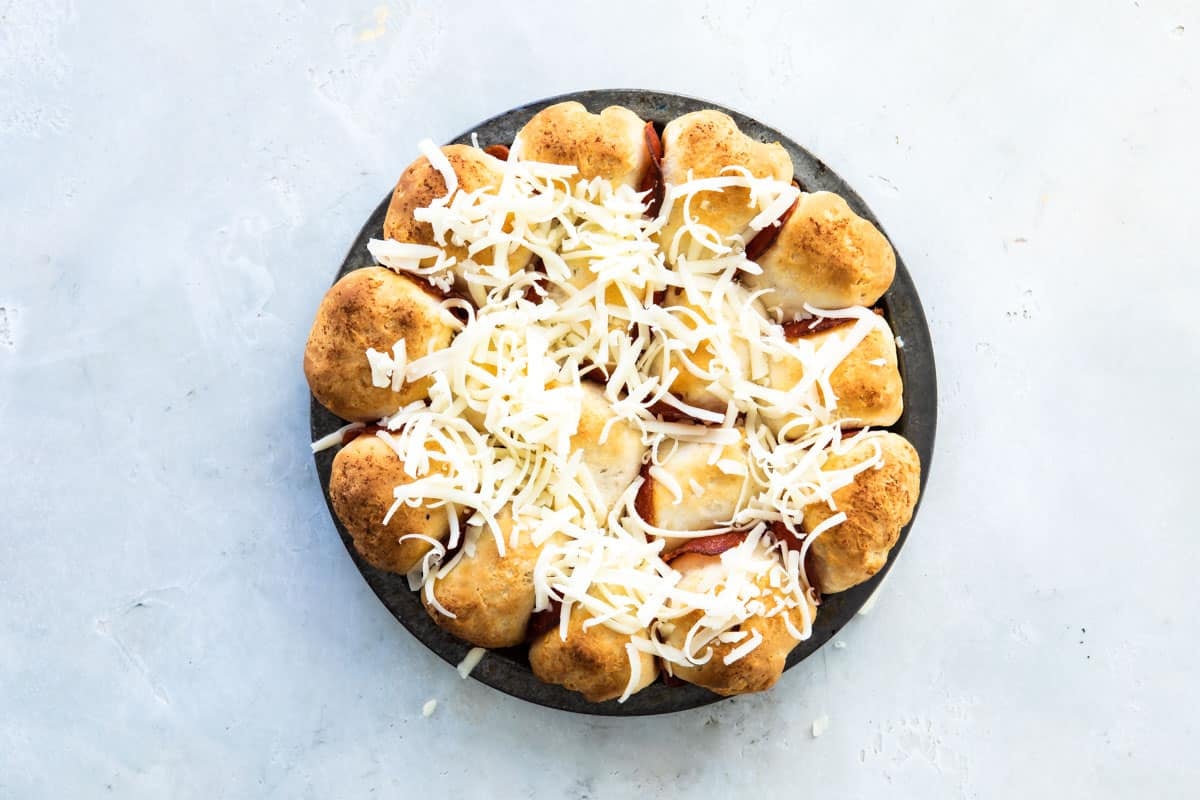 Pepperoni pizza bites in a dark gray pan before having cheese melted on the top.