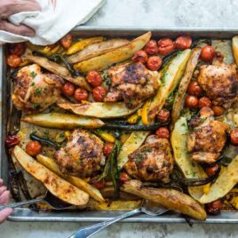 Someone scooping a potato off of a sheet pan filled with vegetables and paprika chicken.
