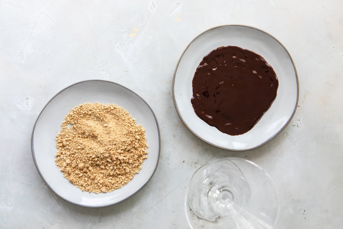 Shallow dishes with chocolate syrup and graham cracker crumbs next to a martini glass.