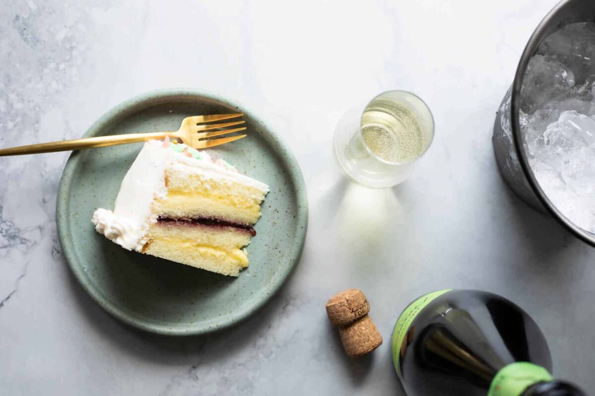 A bottle and flute of champagne next to a plate of Danish layer cake.