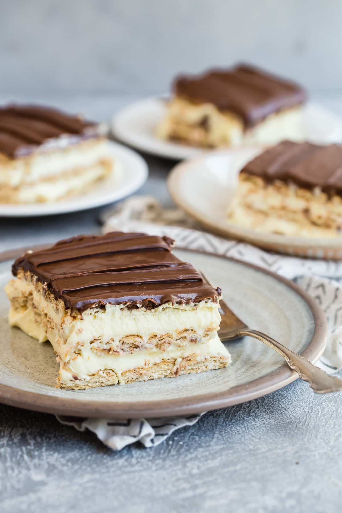 Slices of no-bake Chocolate Eclair Cake on white plates with forks.