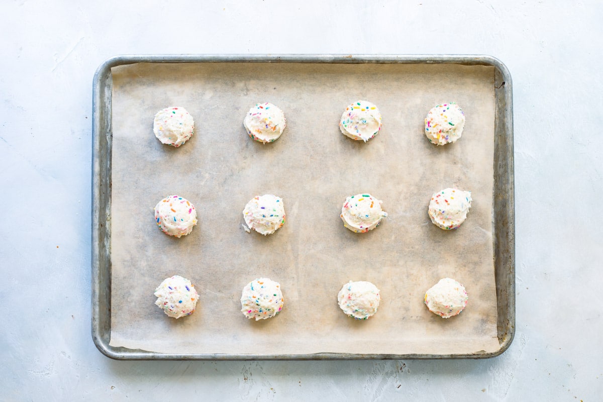 Twelve Confetti cookie dough balls on a baking sheet before being baked.