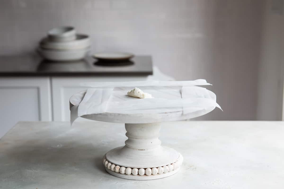 Prepping a cake stand with parchment before decorating a cake.