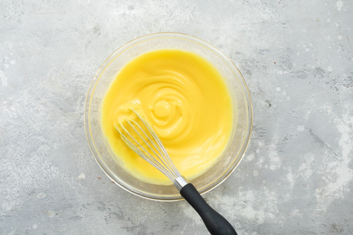 Vanilla pudding in a clear bowl with a whisk.