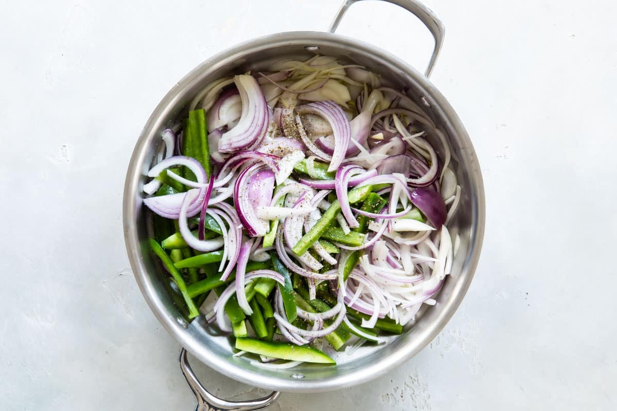 A skillet full of sliced green bell peppers and red onions for fajitas.