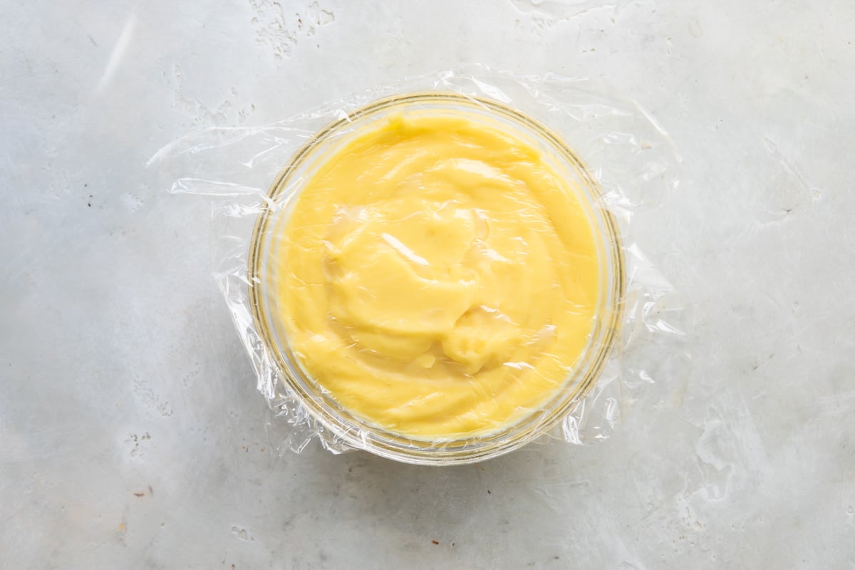 A clear bowl of pastry cream covered with a layer of plastic wrap.