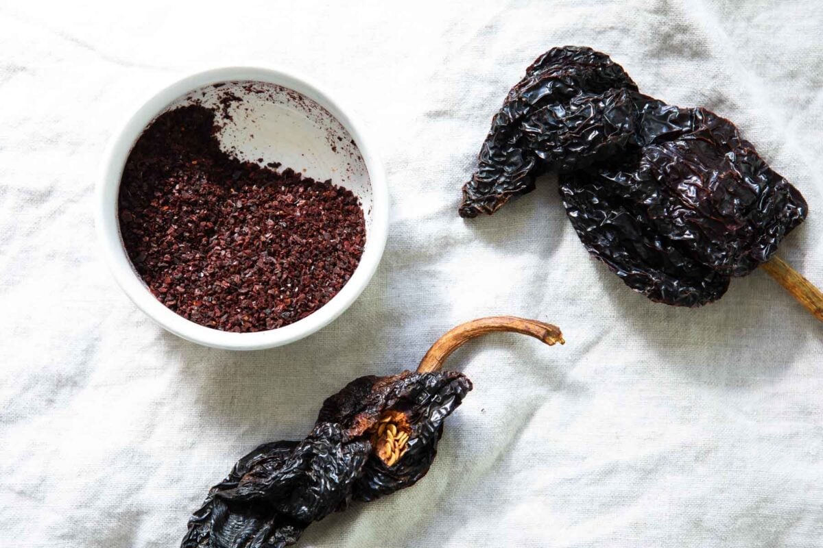 A bowl of ancho chile powder next to dried ancho chiles.