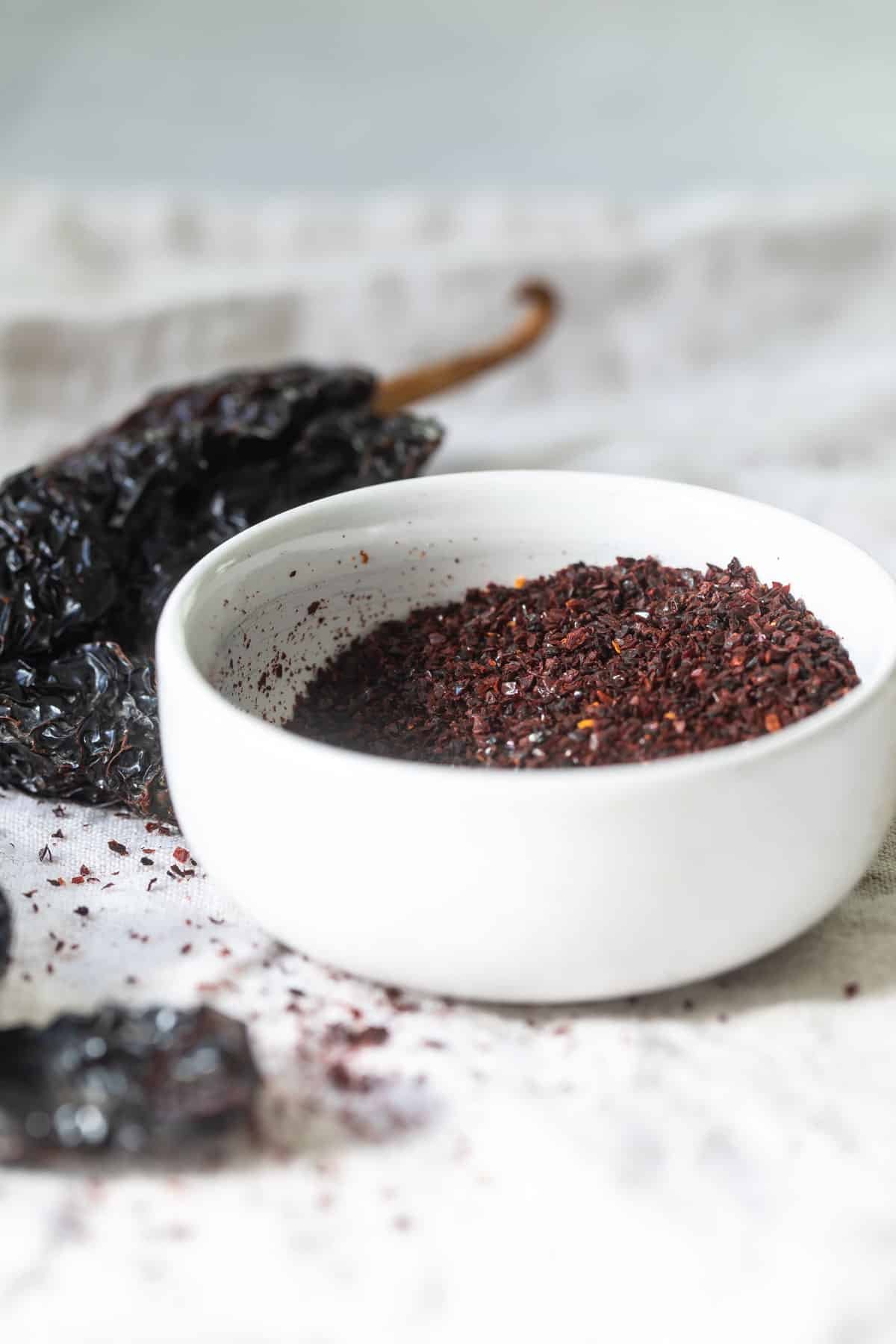 A bowl of ancho chile powder next to dried ancho chiles.