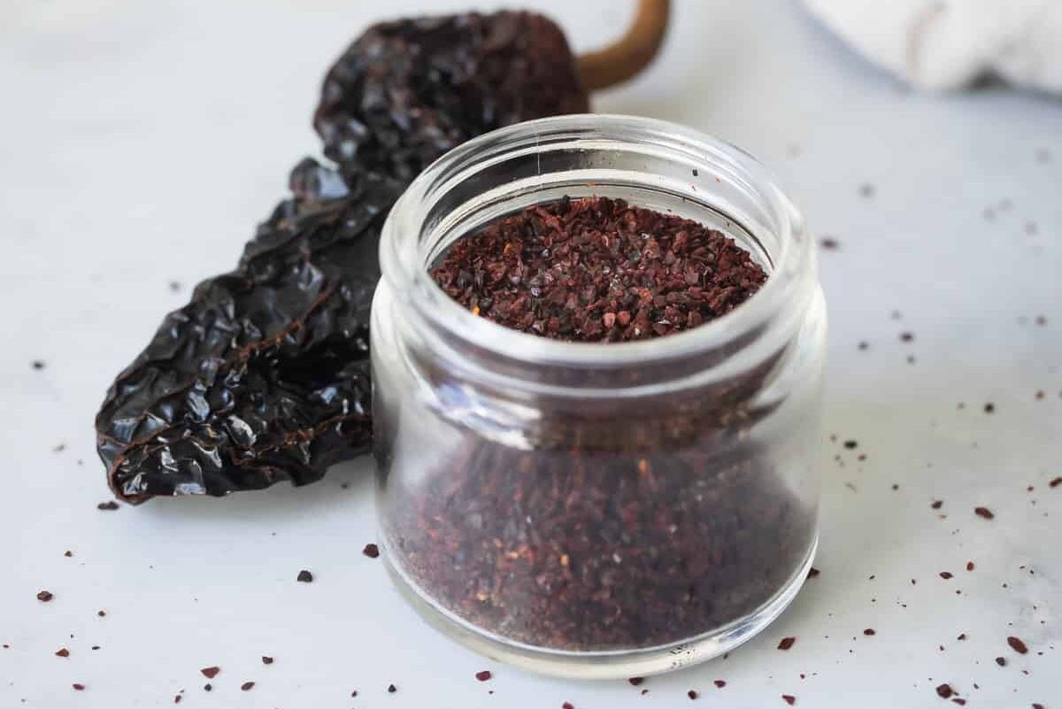 A jar of ancho chile powder next to dried ancho chiles.