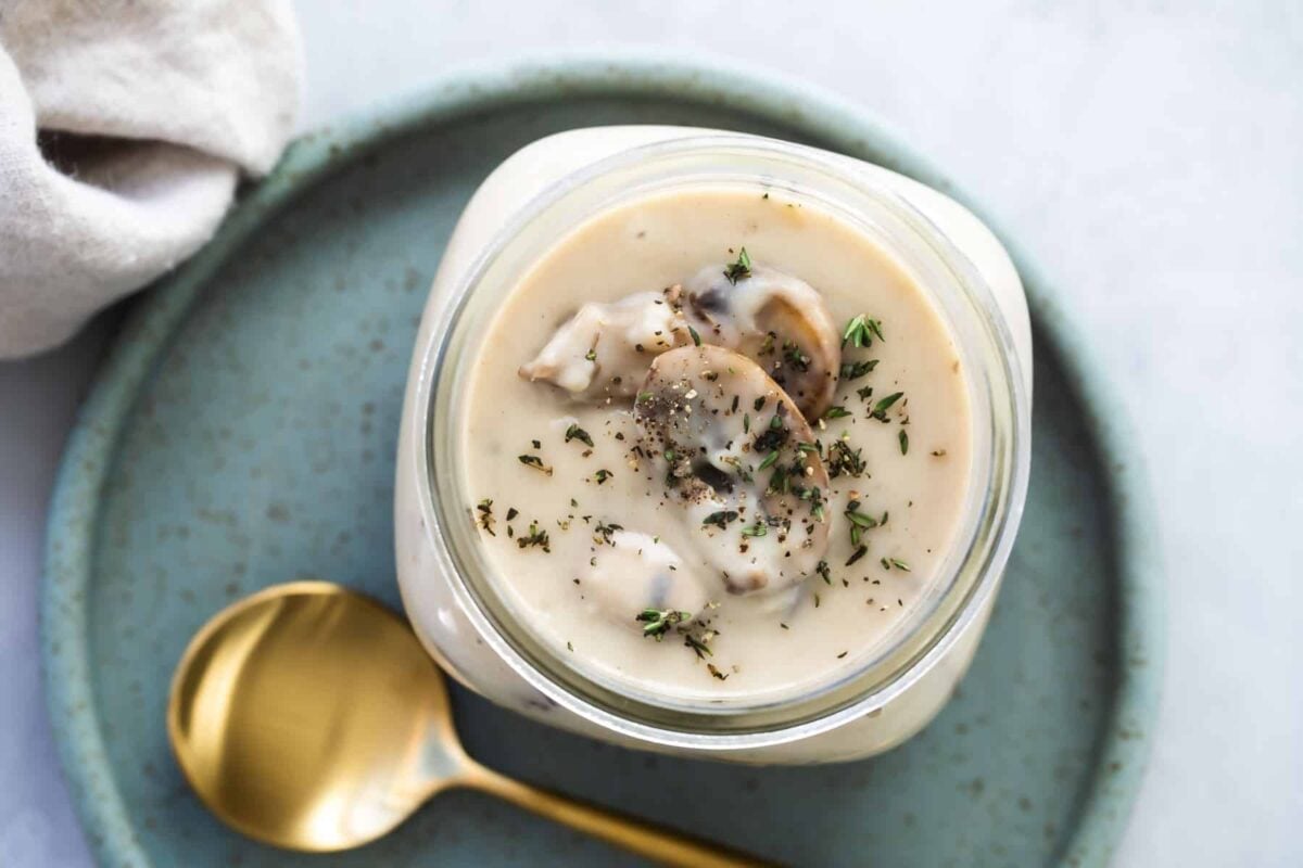 Homemade cream of mushroom soup in a mason jar with a gold spoon resting next to it.