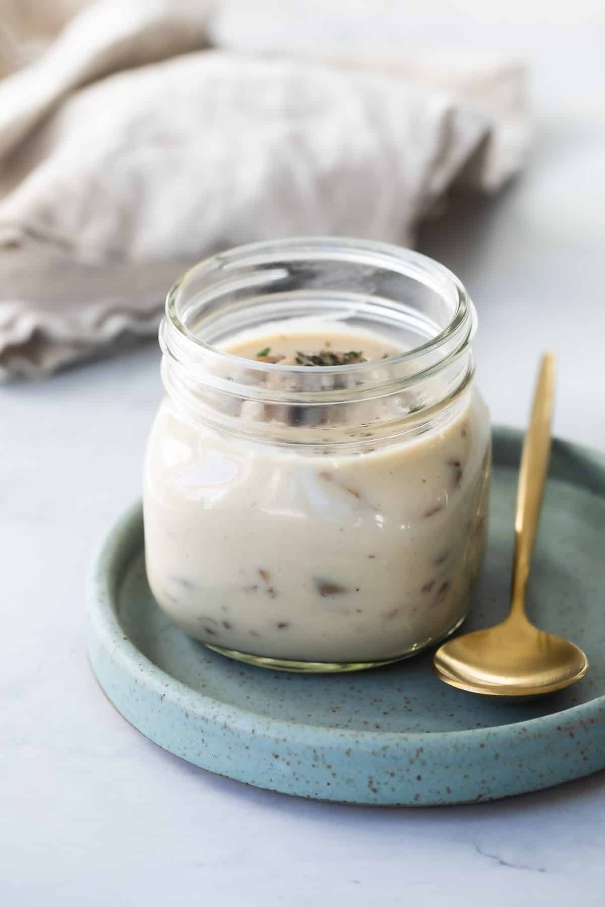 Homemade cream of mushroom soup in a mason jar with a gold spoon resting next to it.