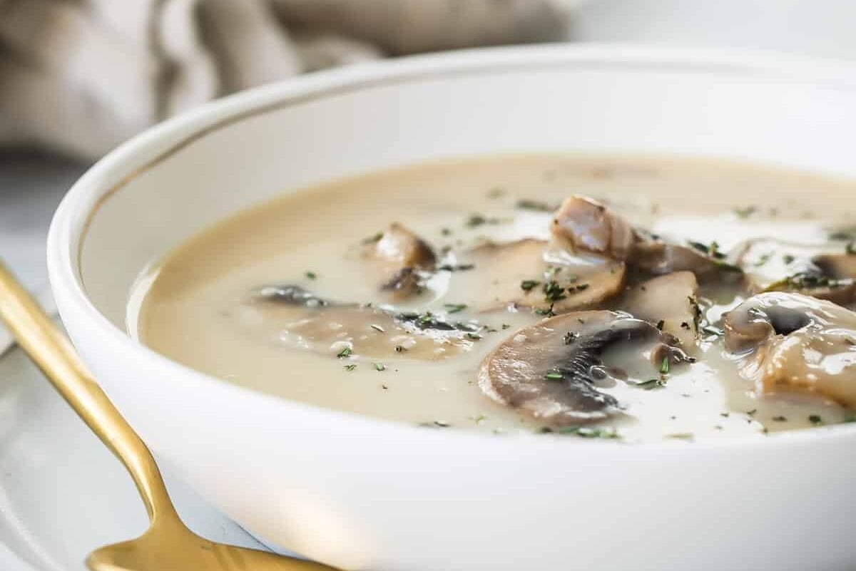 Homemade cream of mushroom soup in a white bowl with a gold spoon resting next to it.