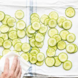Cucumber slices being patted dry with a towel.