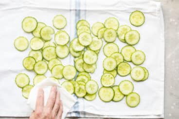 Cucumber slices being patted dry with a towel.