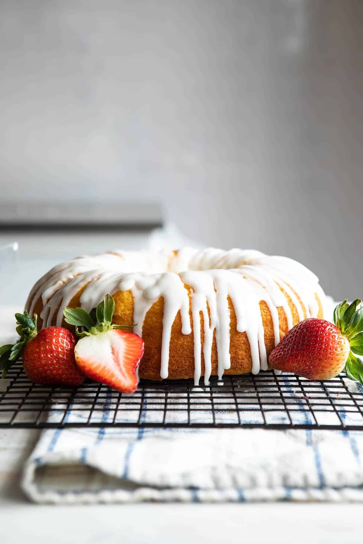 An unsliced lemon bundt cake with lots of glaze and some strawberries nearby.
