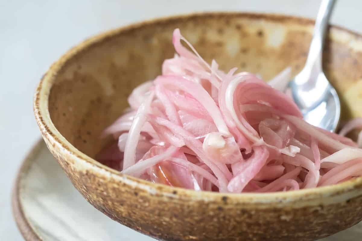 A bowl of pickled shallots with a spoon inside.
