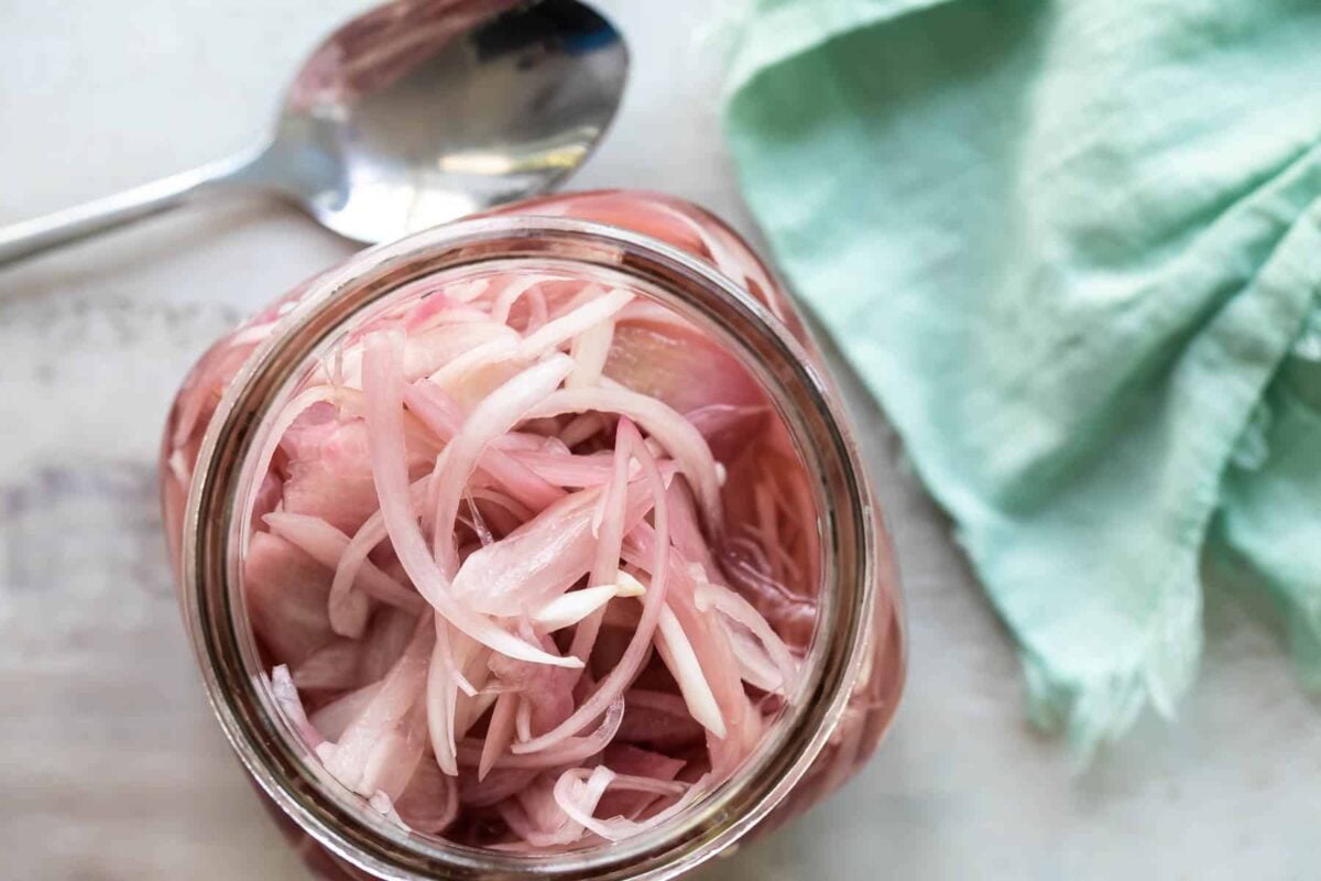 A jar of pickled shallots next to a spoon.