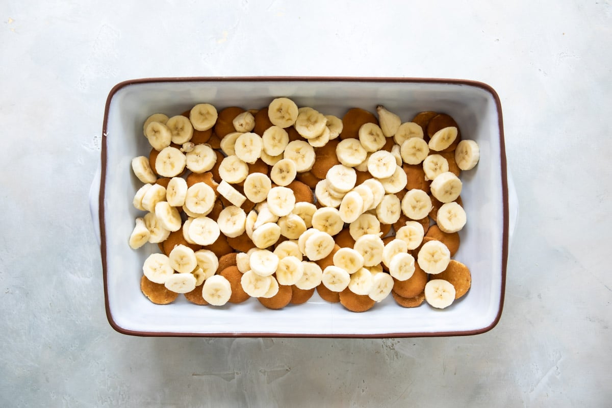 Spreading fresh bananas over wafers in a baking dish.