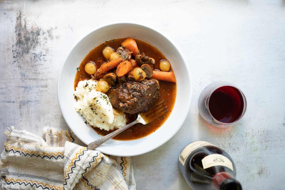A white bowl of beef bourguignon and mashed potatoes.