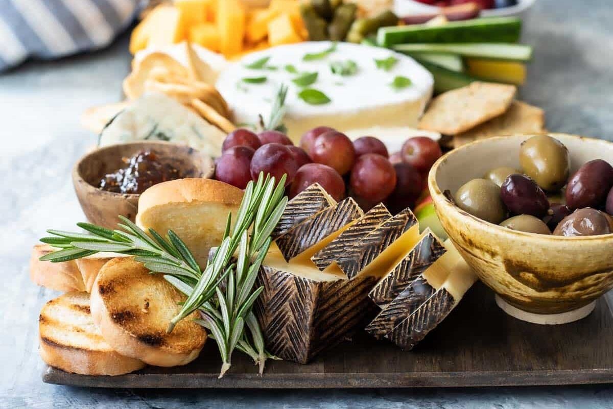 A cheese board filled with fruits, vegetables, nuts, crackers, and cheese.