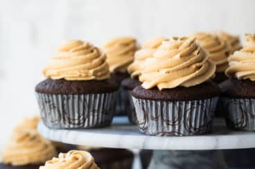 Chocolate cupcakes with peanut butter frosting on a marble cake stand.