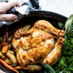 Someone holding a garlic butter roast chicken in a black roasting pan.