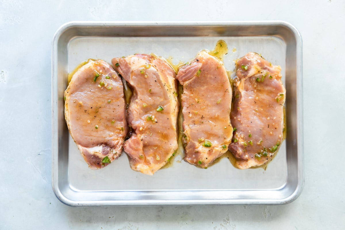 Raw pork chops on a baking sheet.